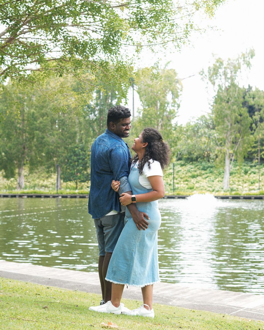 A couple shares a romantic moment by a tranquil lake on a sunny afternoon.