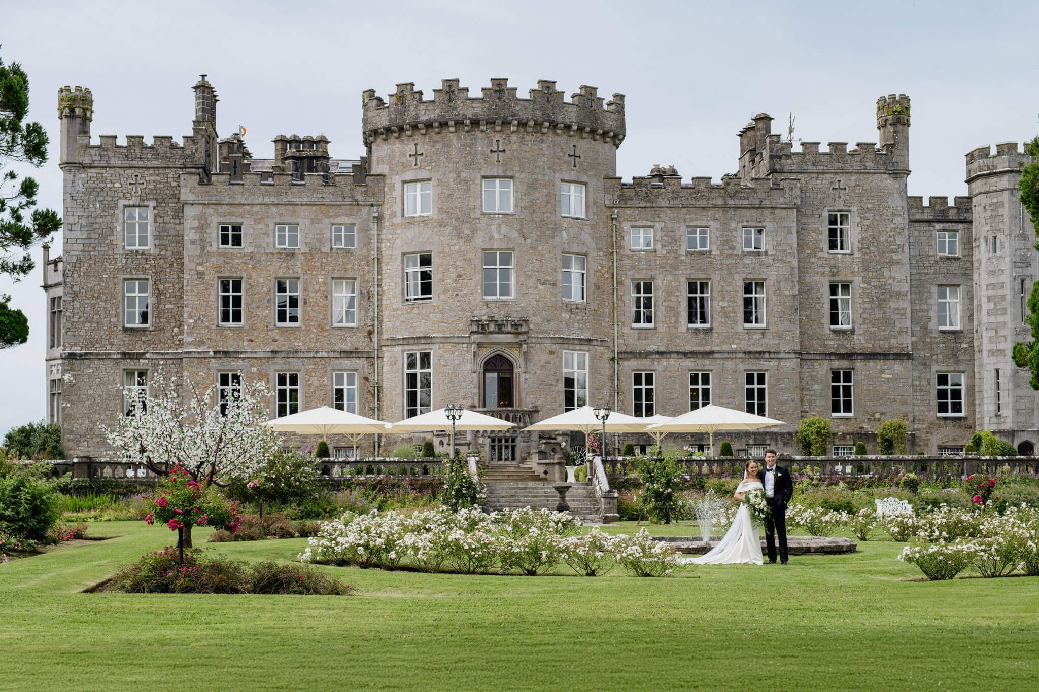 Majestic stone castle Markree castle with turrets and gardens hosting an outdoor wedding reception. Couple posing.