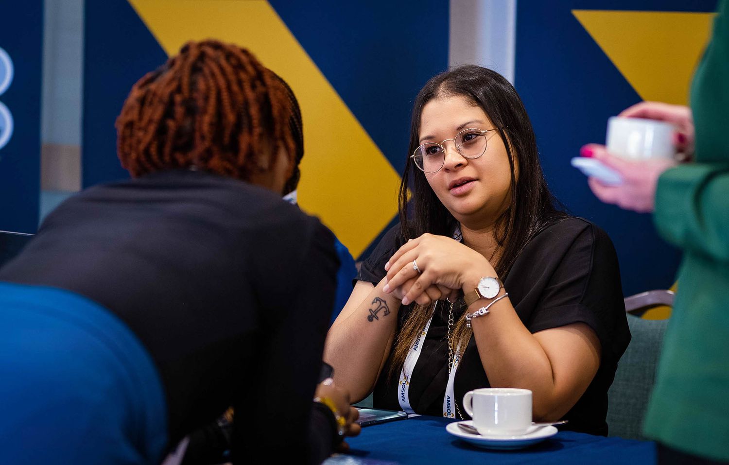 Two people having a conversation over coffee at a table with blue geometric background.
