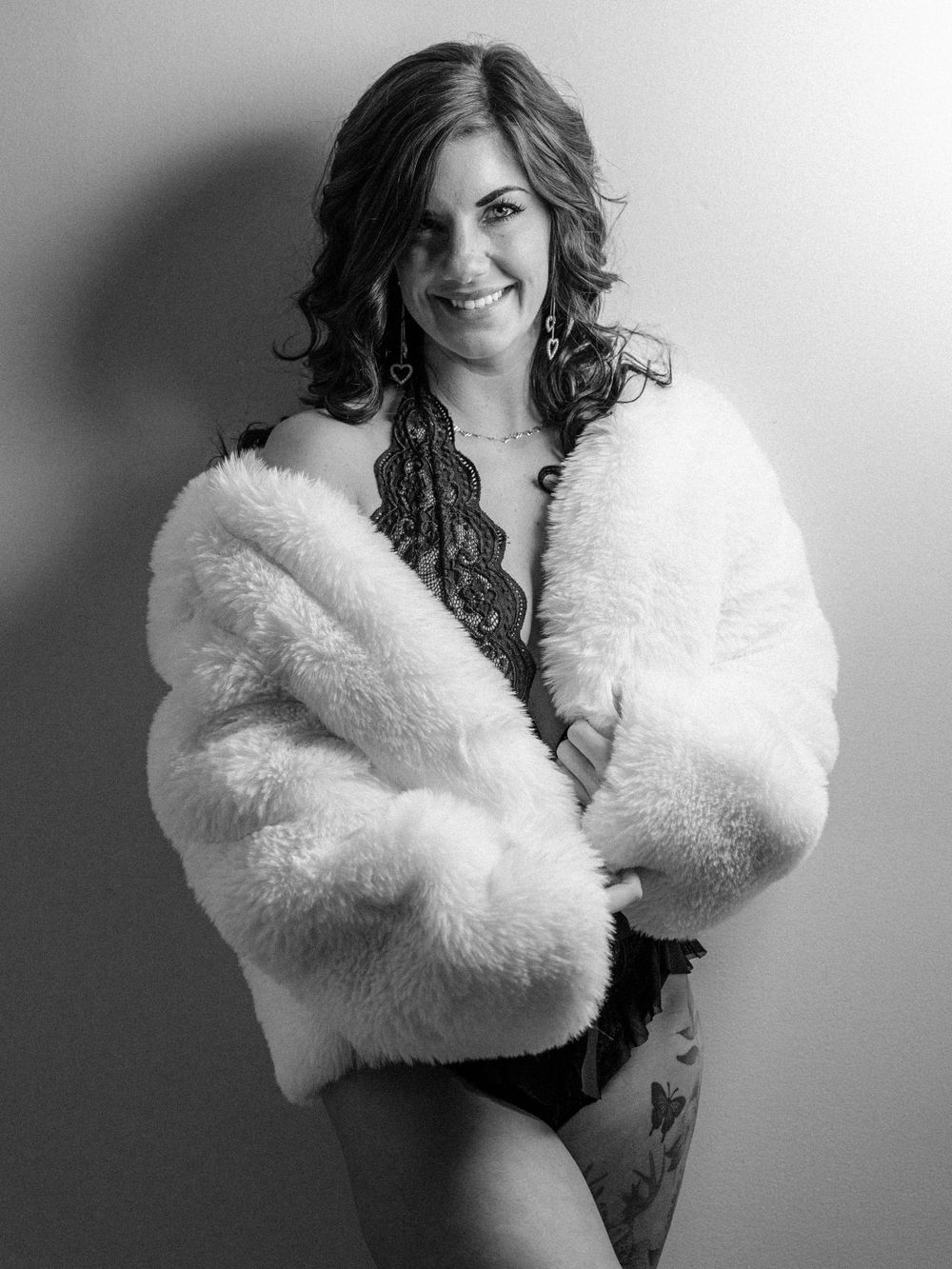 Boudoir photo of a Knoxville woman with a white fur coat  and lace bodysuitposing in East Tennessee boudoir photographer's portrait studio