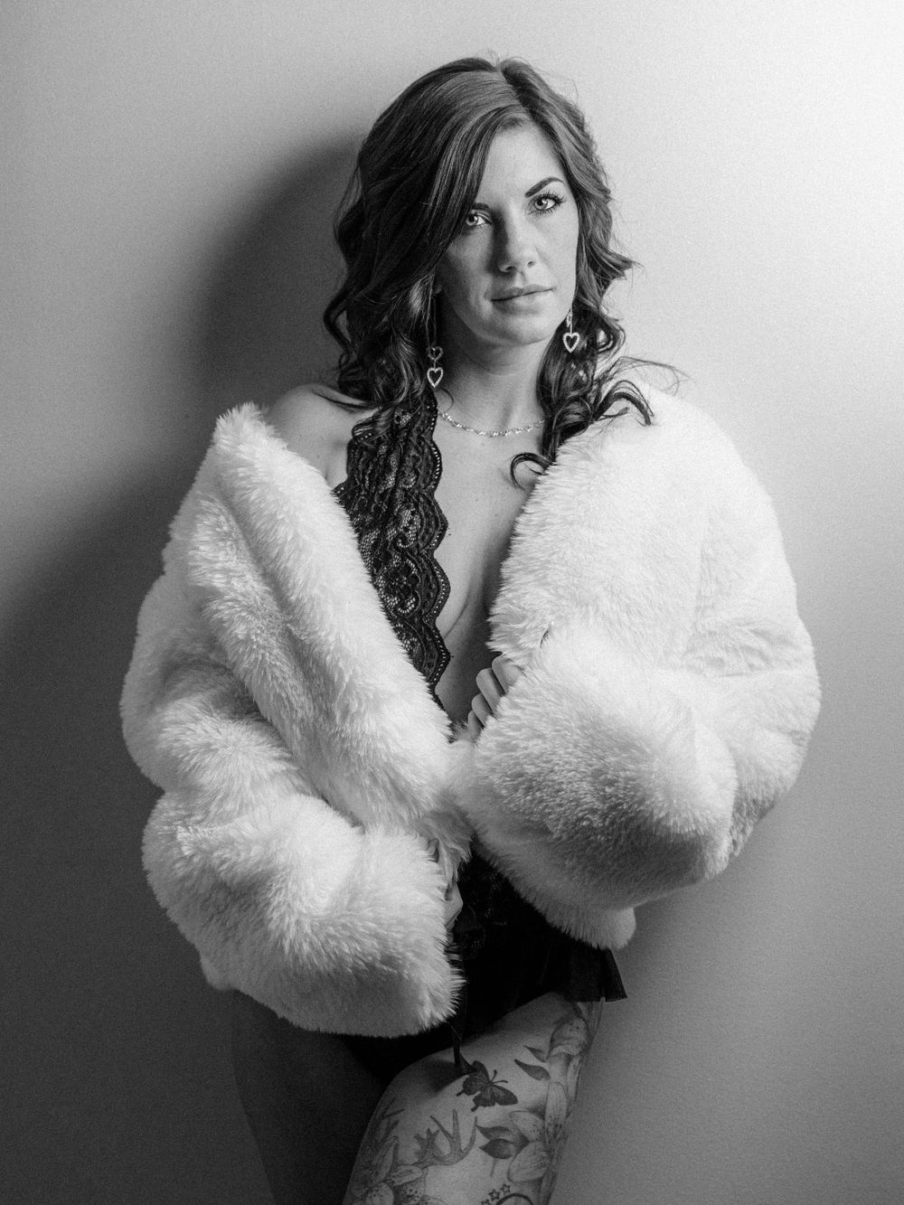 Boudoir photo of a Knoxville woman with a white fur coat and lace bodysuit posing in East Tennessee boudoir photographer's portrait studio