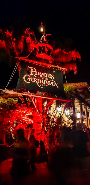The Pirates of the Caribbean ride entrance sign glows in dramatic red lighting at a Disney theme park.