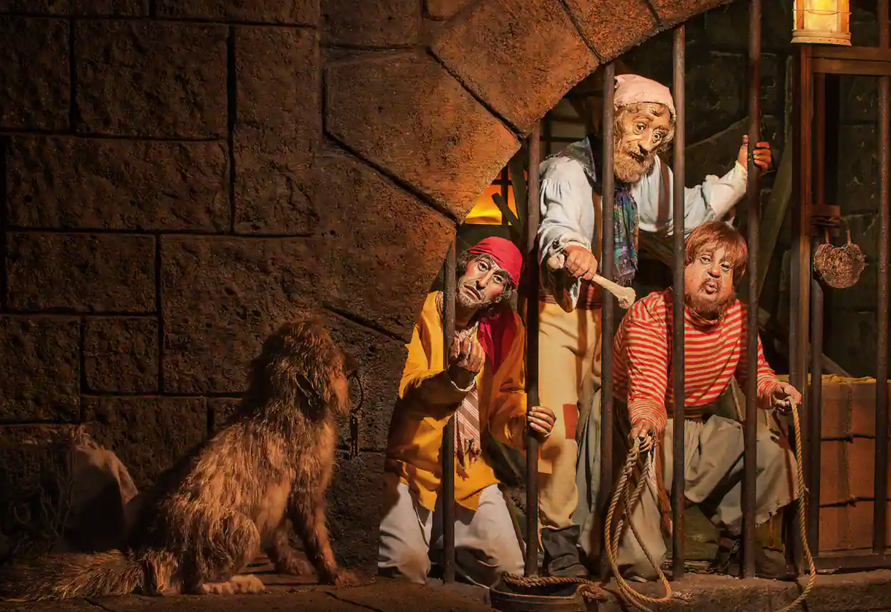 Animatronic figures behind jail bars in the Pirates of the Caribbean ride show prisoners trying to escape with a dog nearby.