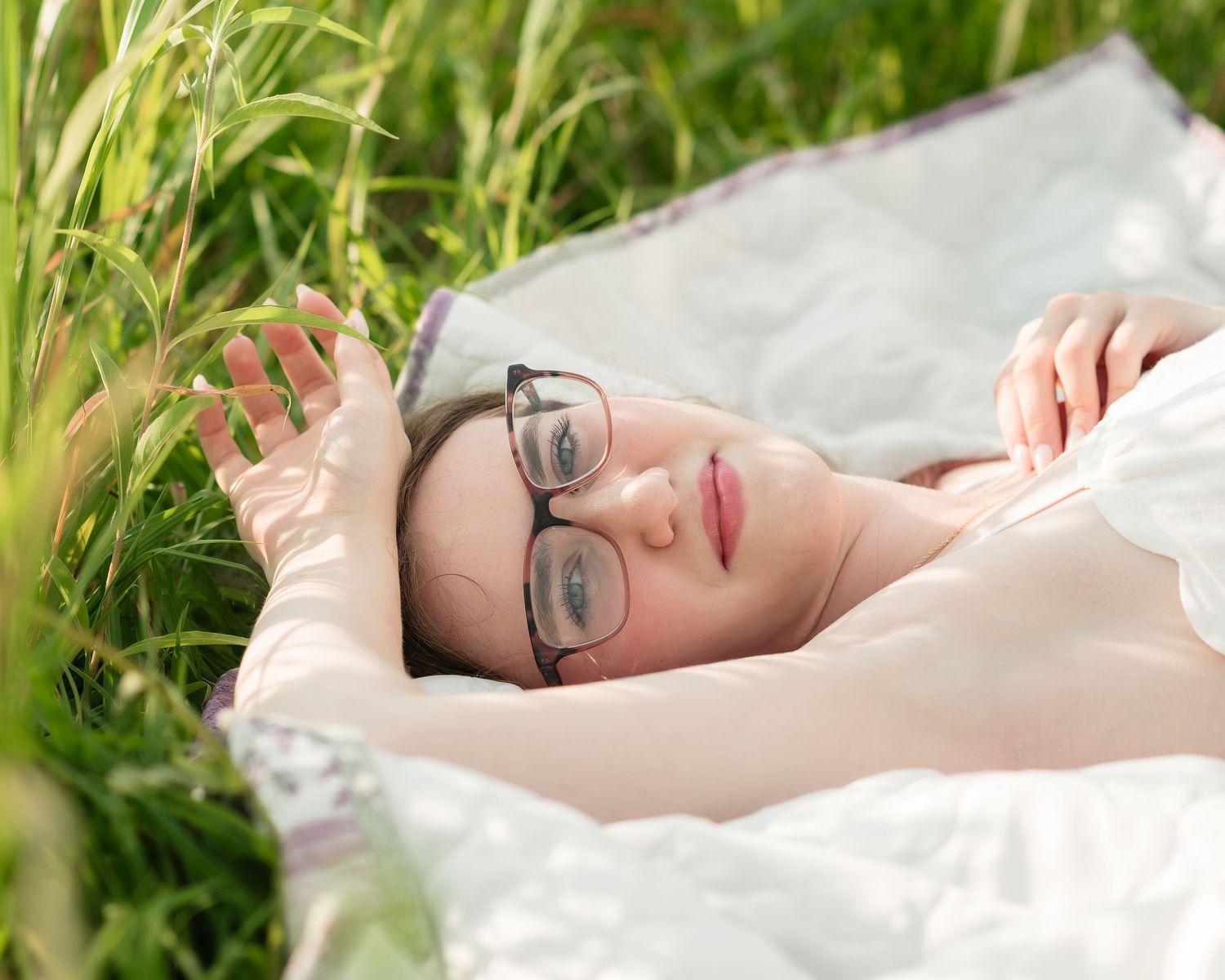 Person lying on grass reading a book in a peaceful forest setting.