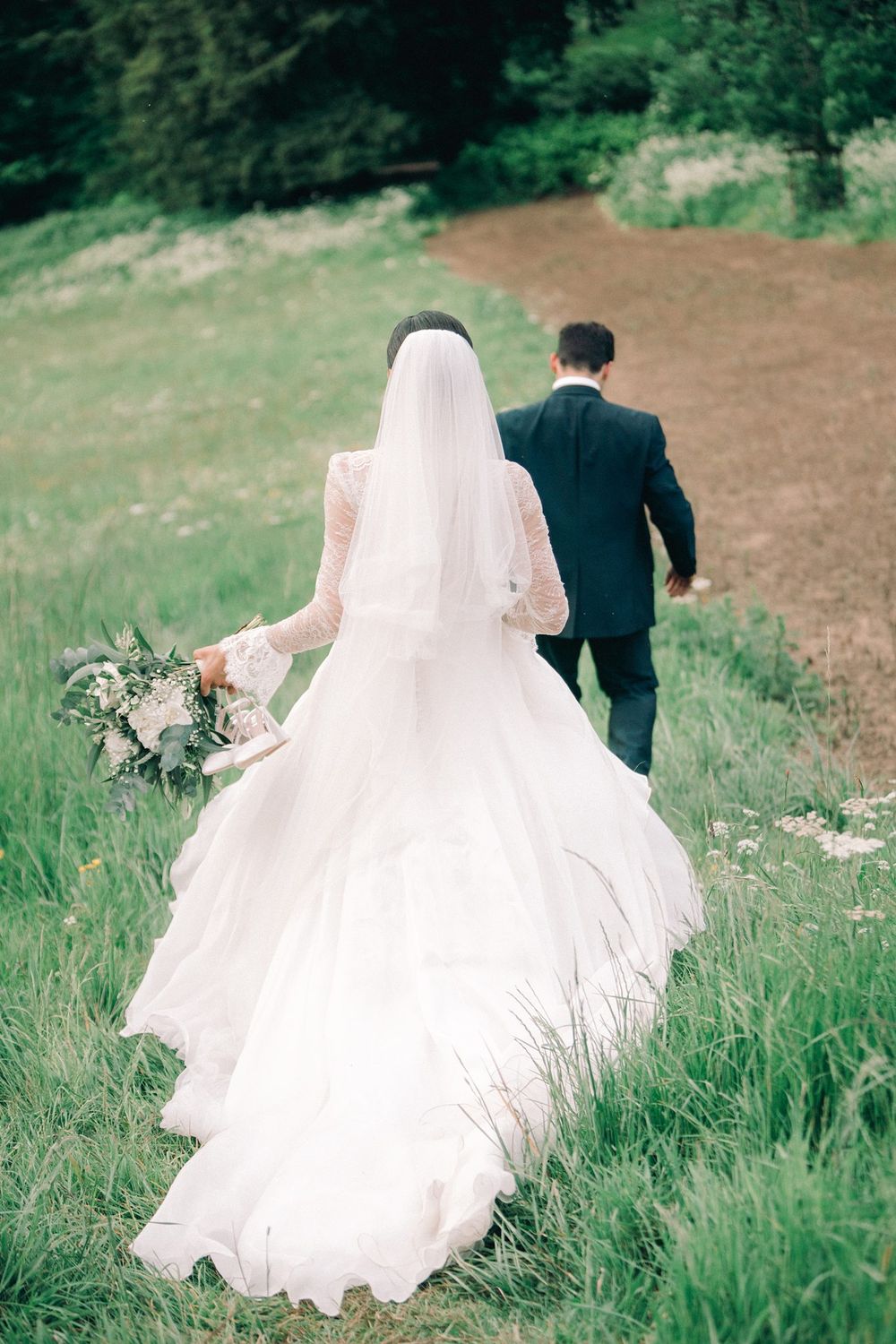 A bride in a flowing white dress and groom in dark suit walk through a grassy meadow on their wedding day. Fox Harb'r Resort wedding photo