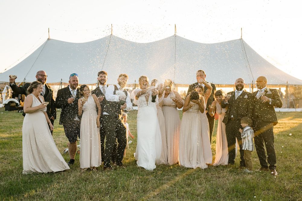 Wedding party celebrates with confetti in front of a white tent at sunset during an outdoor celebration at The Greenhouse on Strawberry Lane