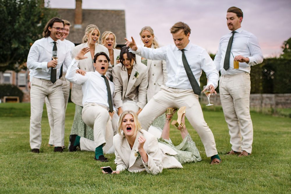 Wedding group strikes playful poses in coordinated white and cream outfits on a garden lawn at Saraguay House Nova Scotia.
