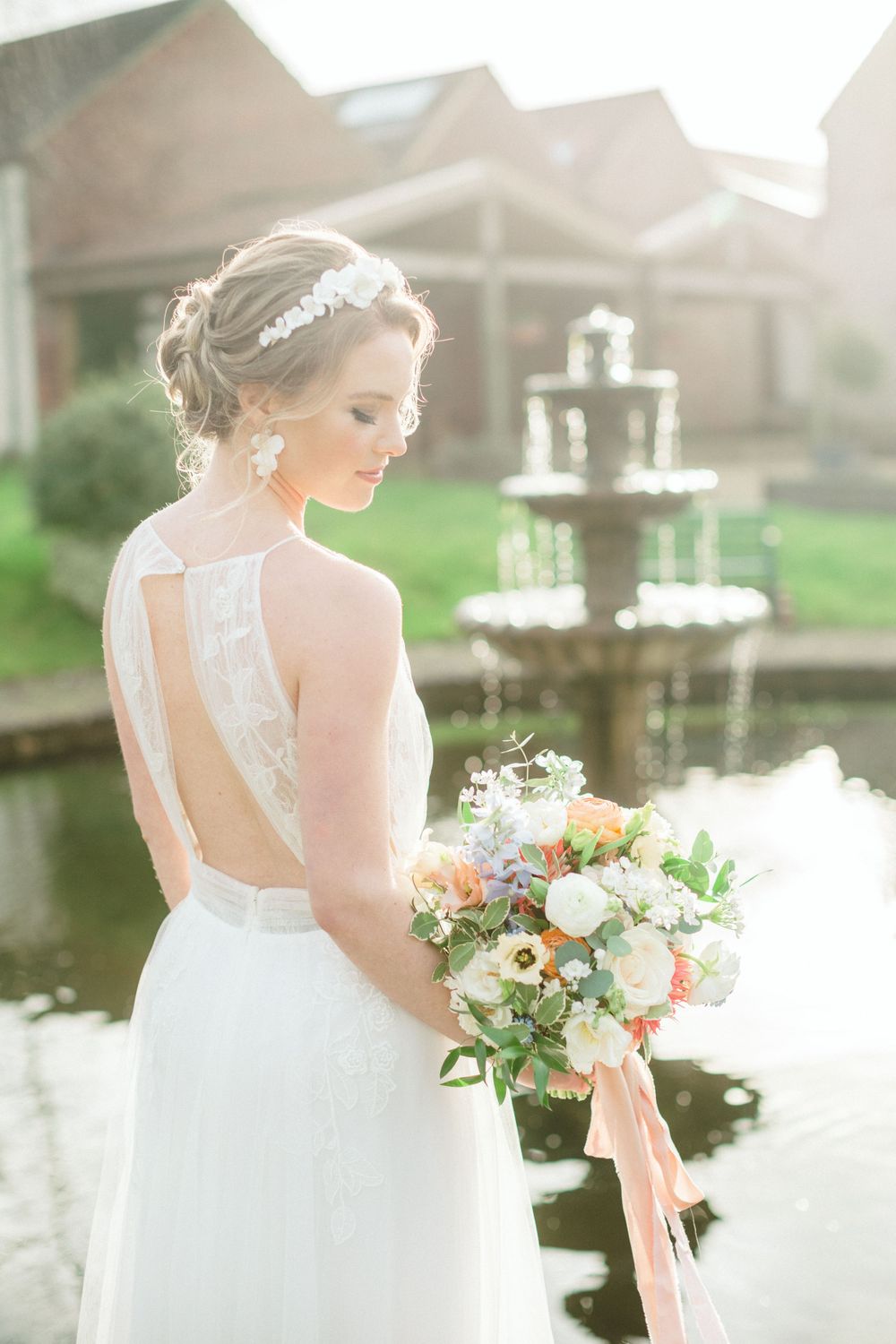 An elegant wedding dress with lace details and open back shown near a fountain in soft natural light in Saraguay Nova Scotia wedding photo.