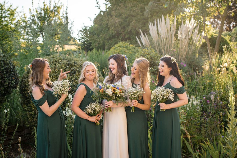 Wedding party in emerald green dresses stands together in a garden setting during golden hour at Hillsdale House, Nova Scotia
