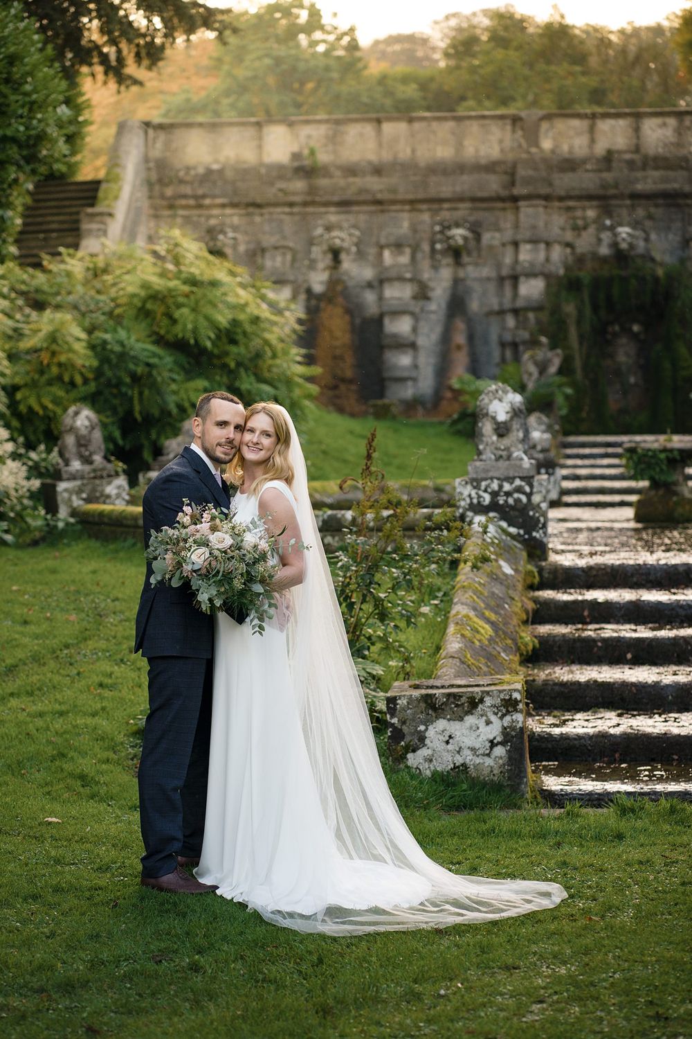 A couple poses for wedding photos in front of an elegant old stone staircase in a garden setting, Nova Scotia wedding photographer