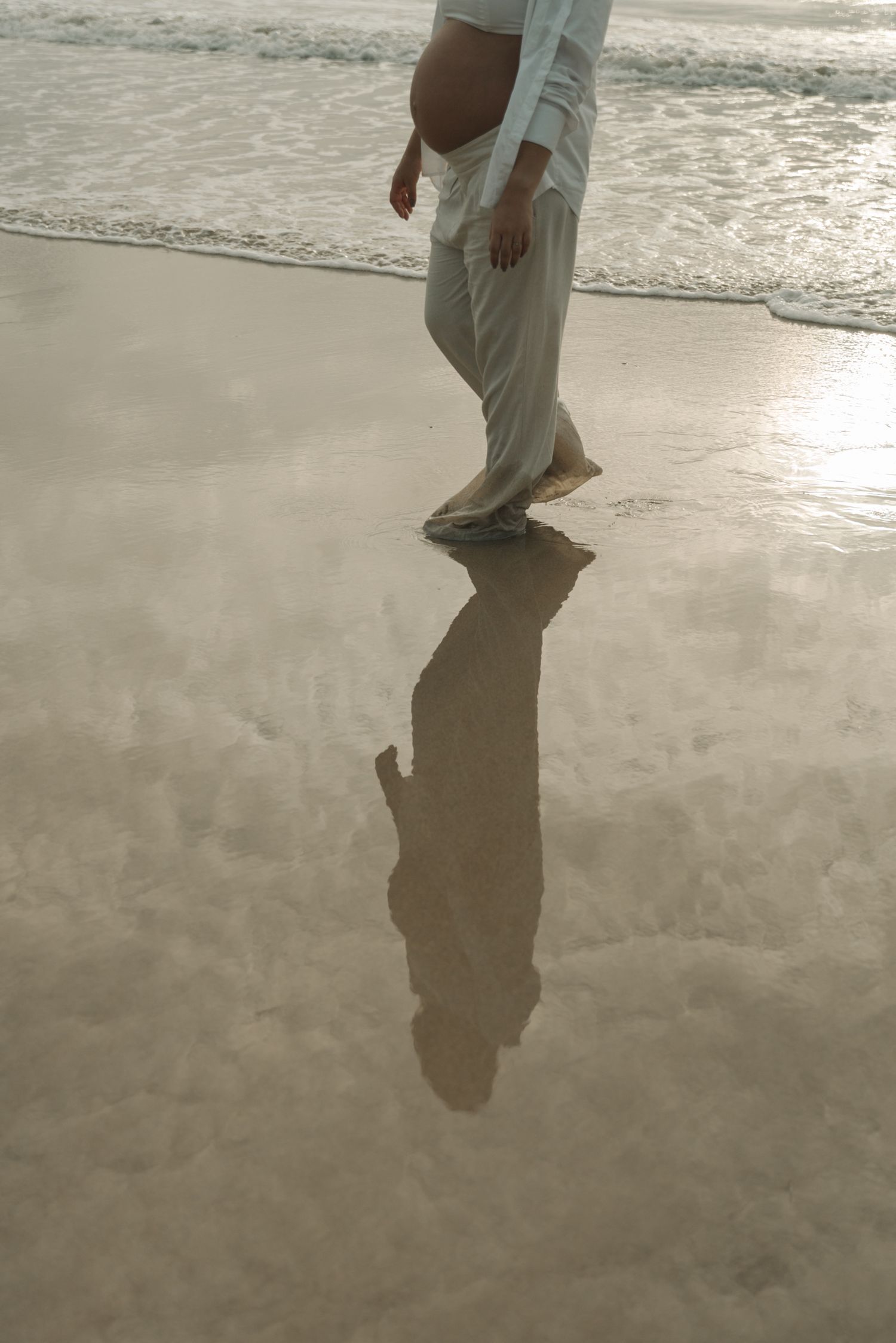 Person's reflection cast on wet beach sand during golden hour.