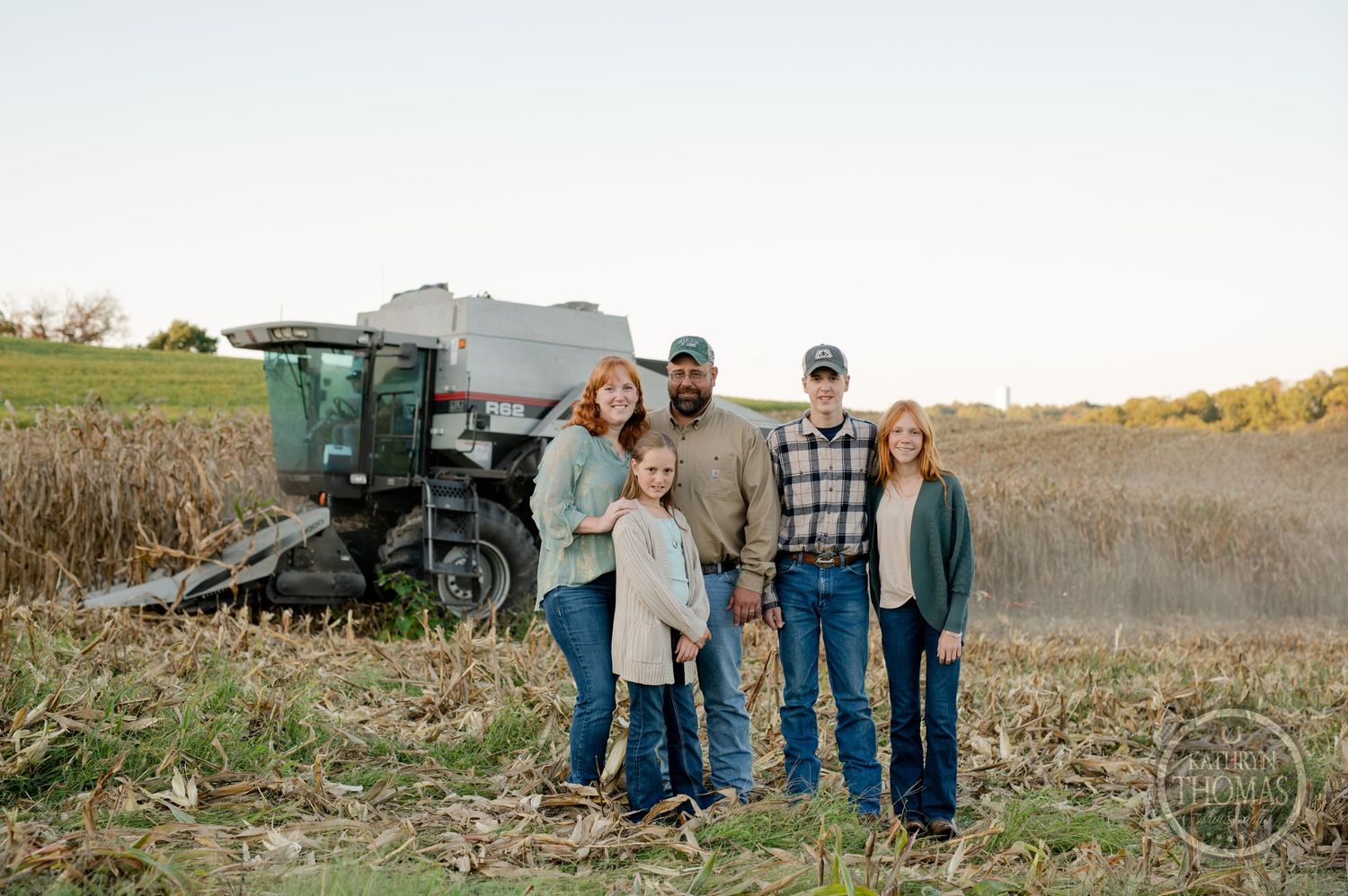 Family group photo with farming equipment in the background during harvest season.