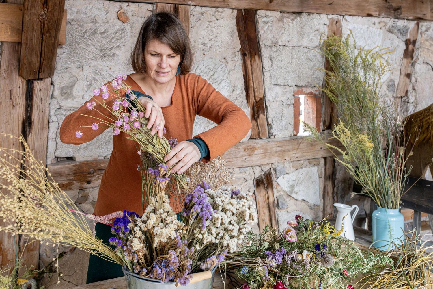 Bild einer Businessreportage, das eine selbstständige Frau zeigt, die einen Trockenblumenstrauß in rustikalem Ambiente arrangiert.