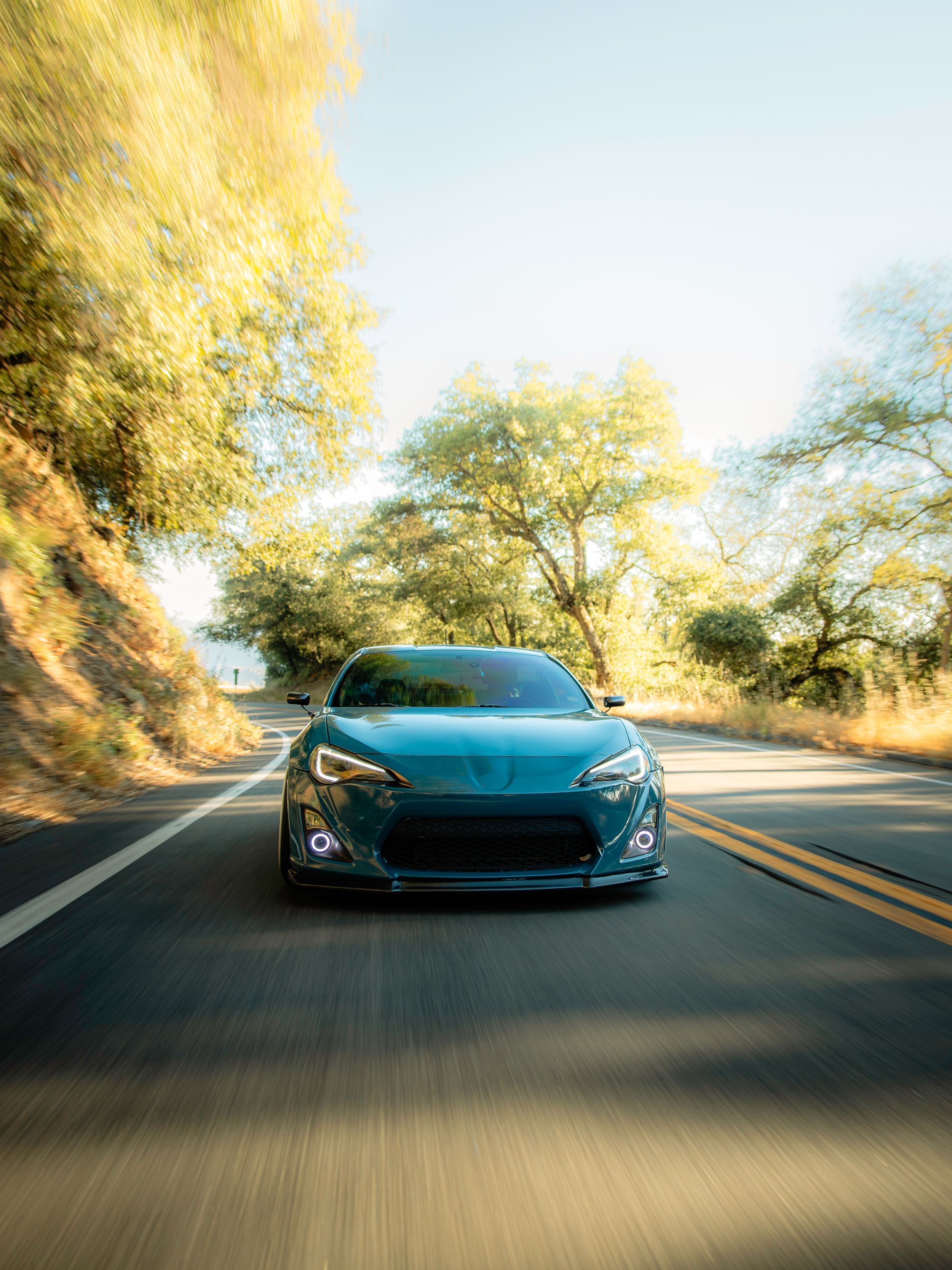 A teal Toyota GT86 at sunset driving through a winding mountain road.