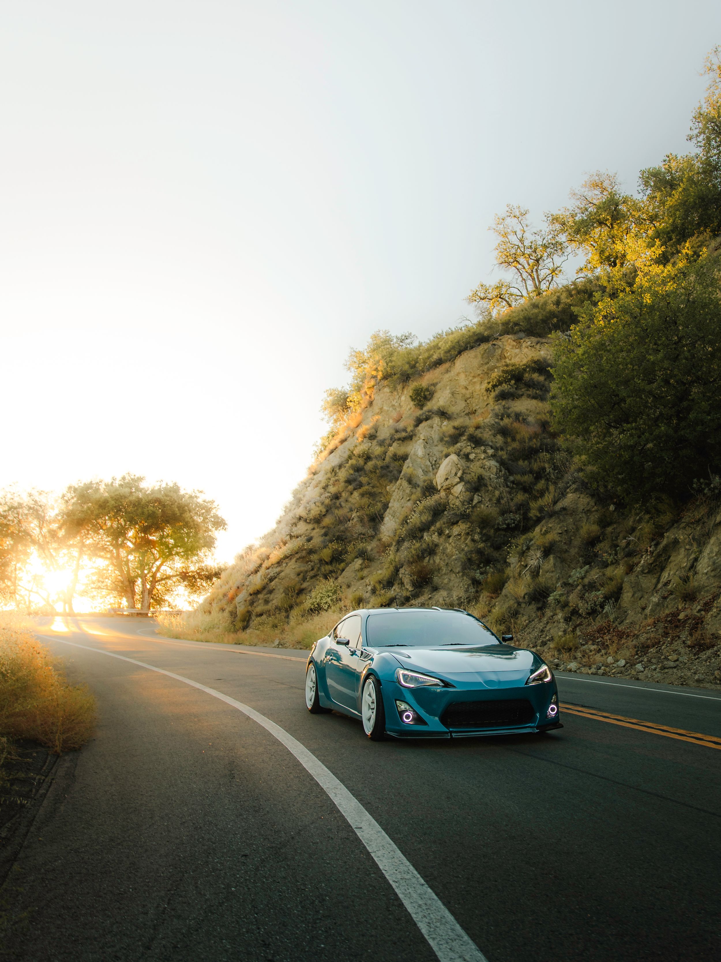 A teal Toyota GT86 at sunset driving through a winding mountain road.