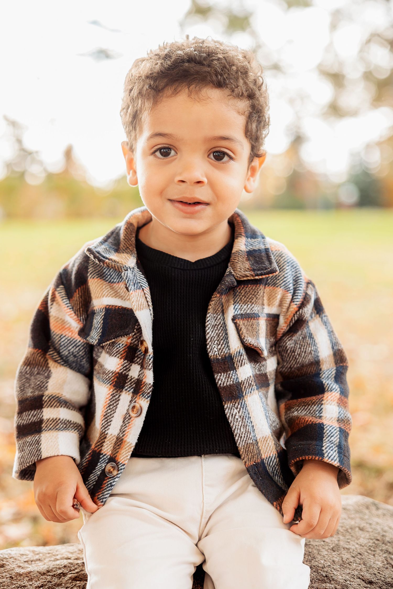 A child wearing a plaid jacket sits outdoors during autumn. Michigan Detroit Novi Northville Portrait Photographer
