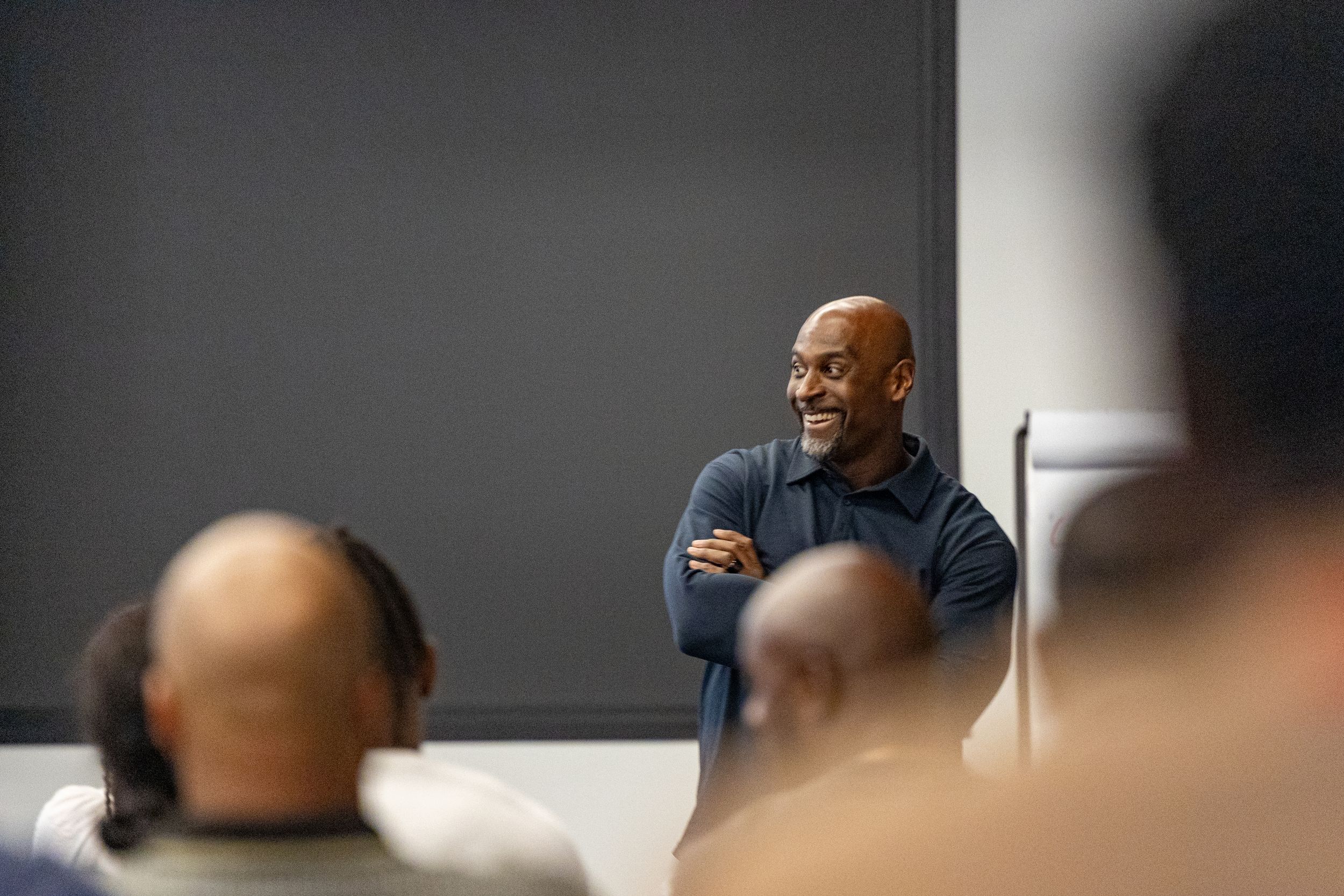 Speaker presenting to an audience in a dark conference room setting.