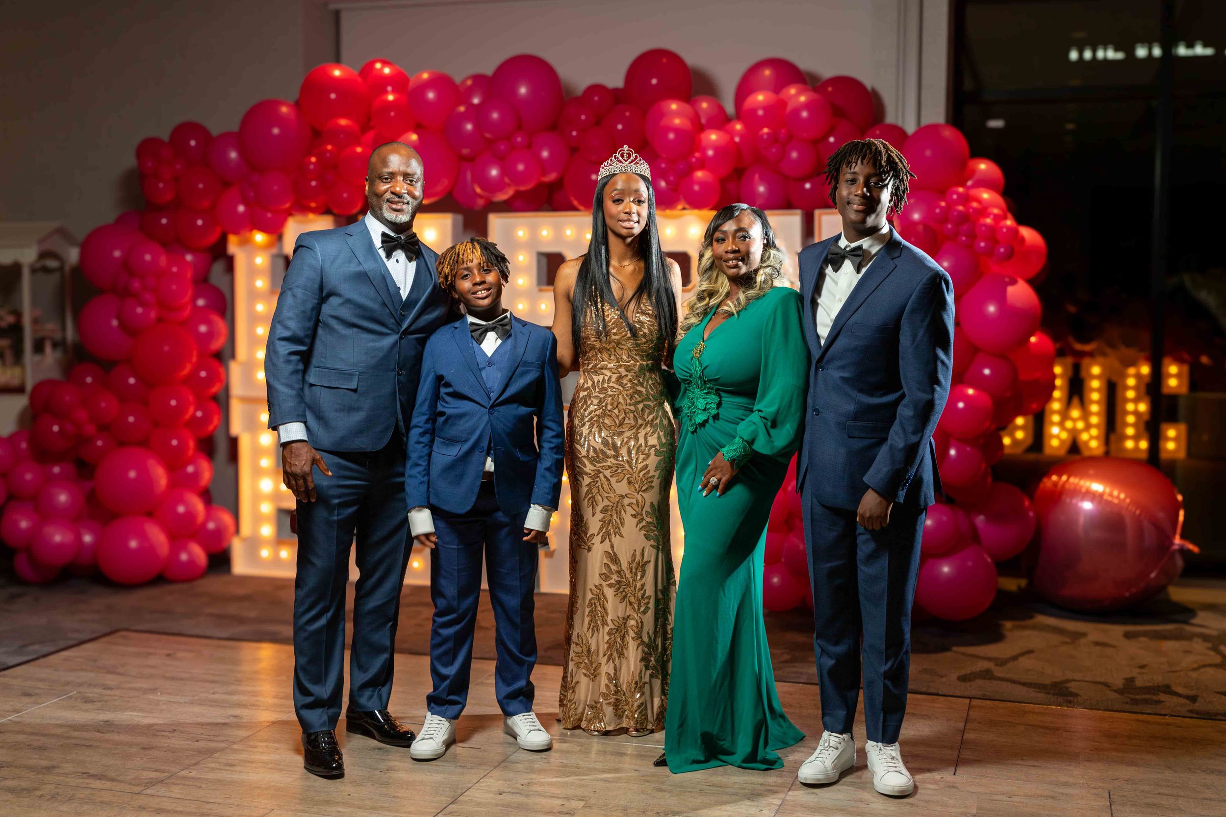 A family of five poses together in front of a festive red balloon arch at an event.