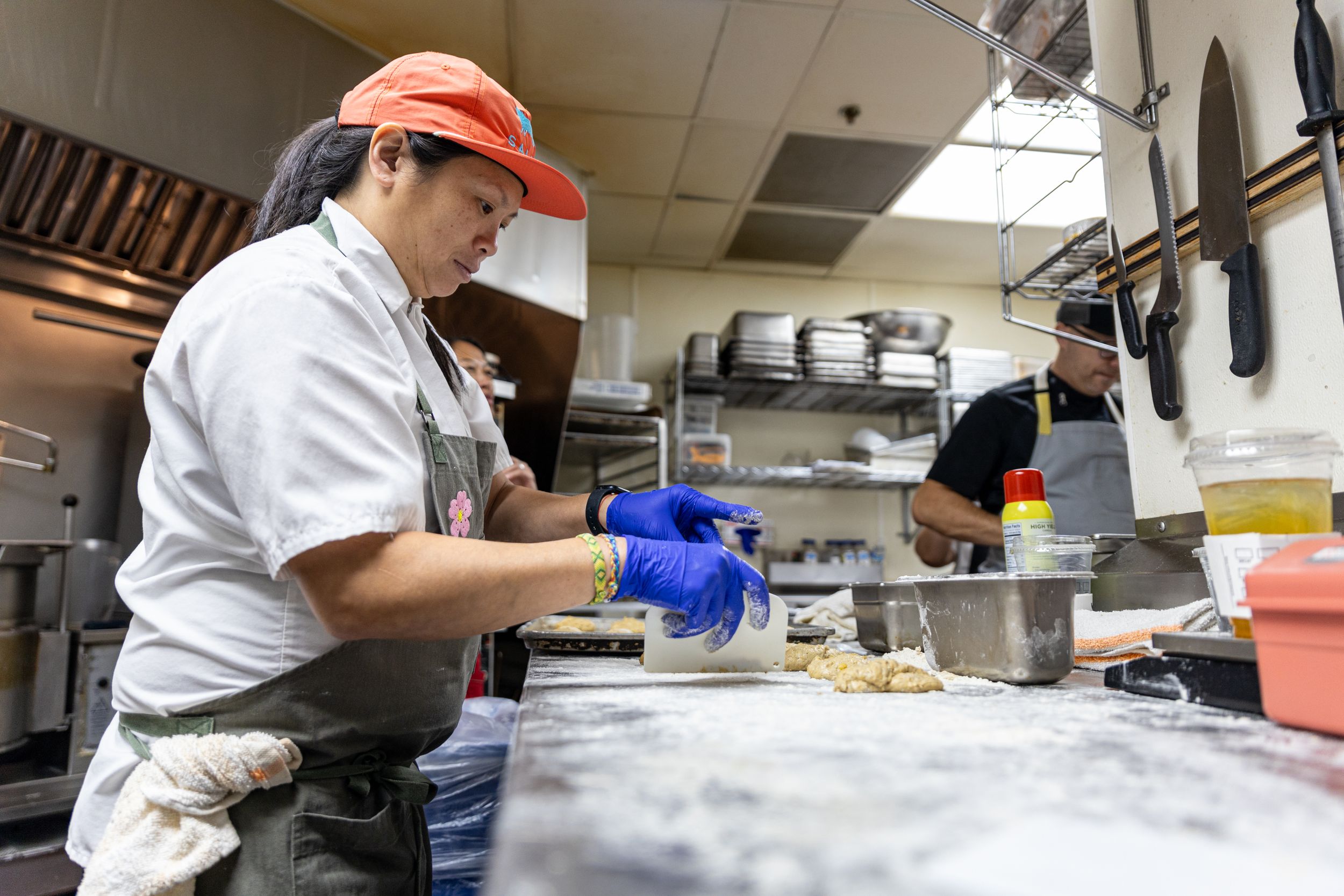 A chef wearing a red visor and gloves prepares food in a commercial kitchen.