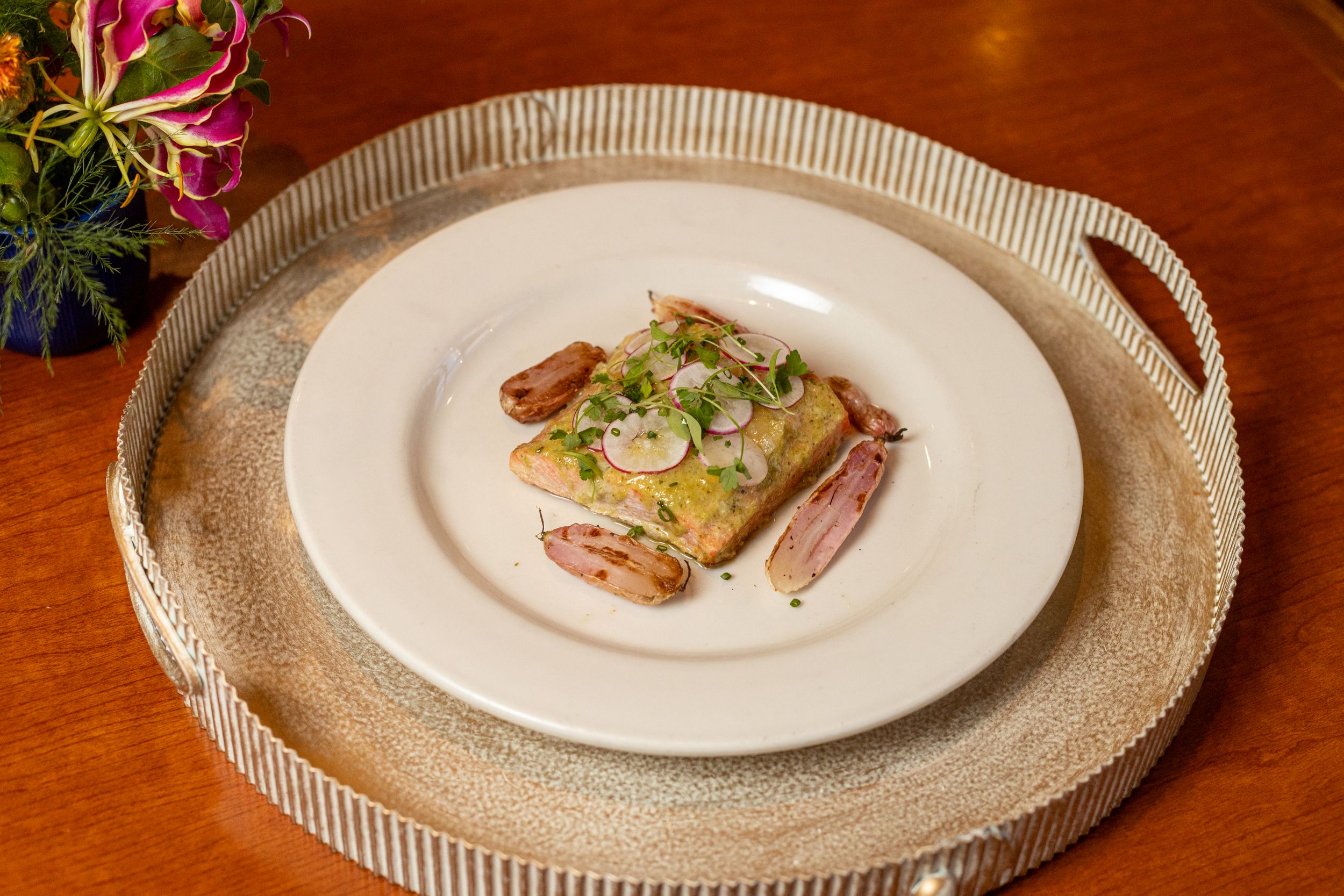 An elegantly plated seafood dish served on a white plate with a decorative silver tray.