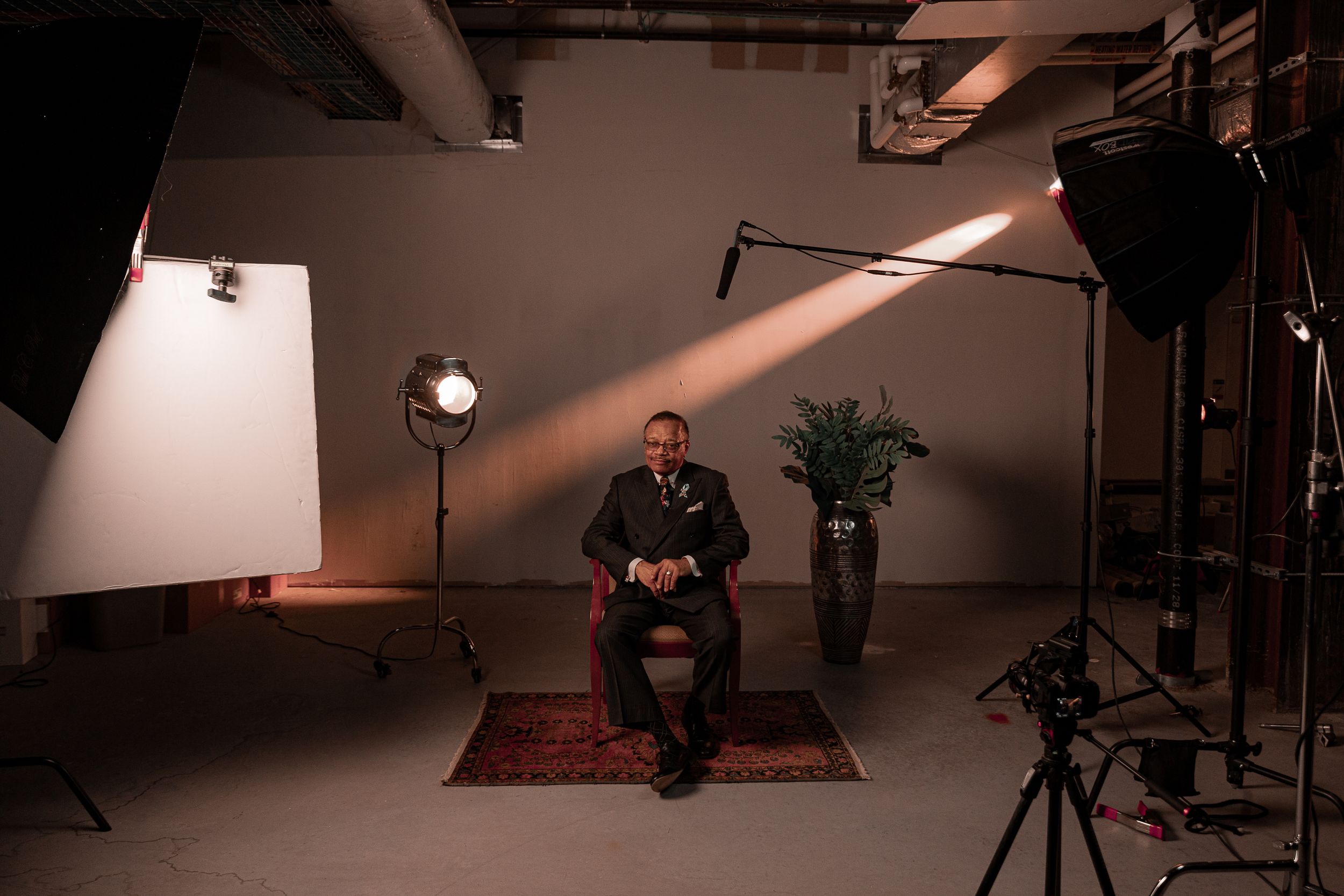 A photography studio setup with dramatic lighting, featuring a chair, rug, and camera equipment.