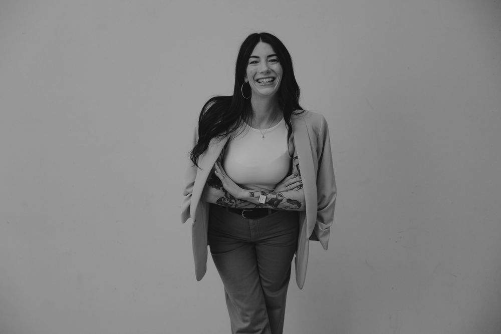Black and white portrait of someone in a blazer and jeans walking against a plain backdrop.
