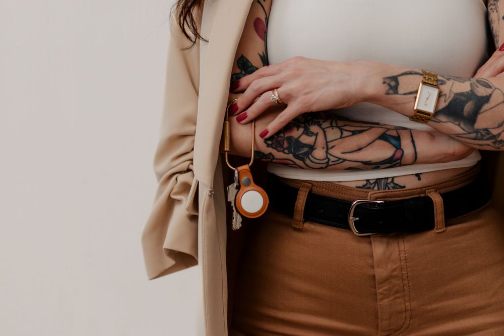 Close-up view of a brown leather belt and beige jacket with tattoos visible on a person's hand.