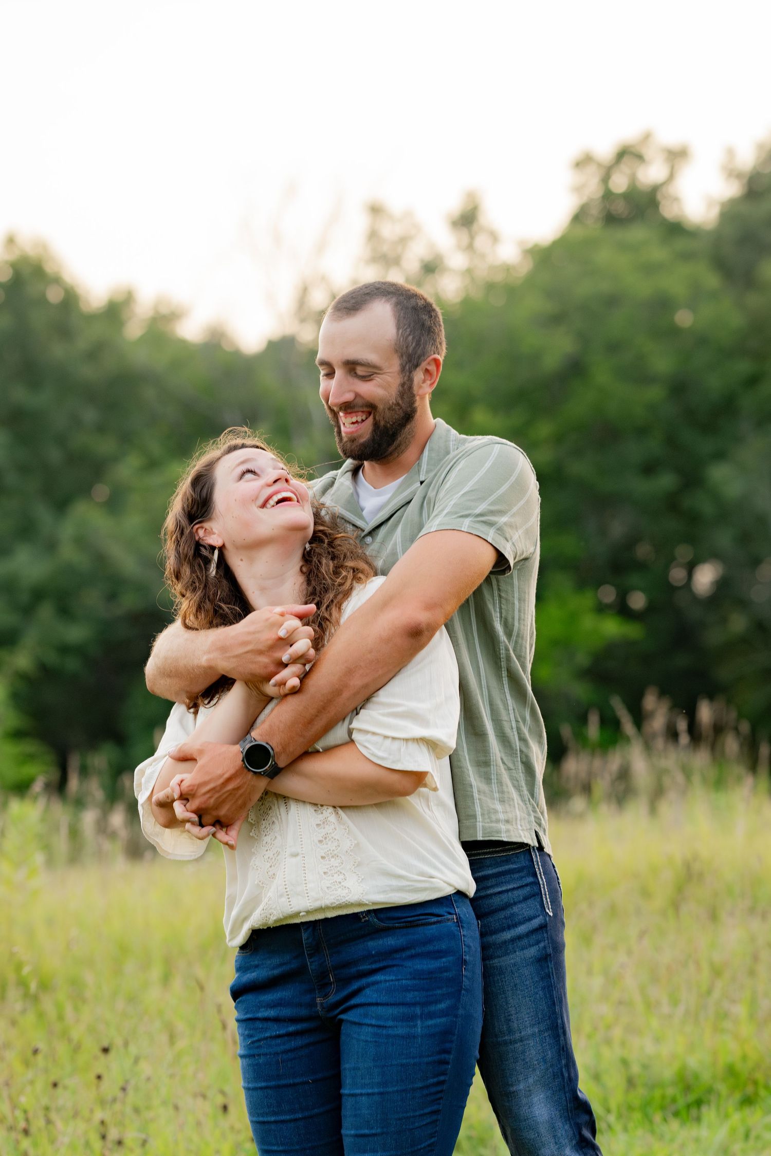 A romantic couple embracing and laughing together in a sunlit meadow during golden hour.