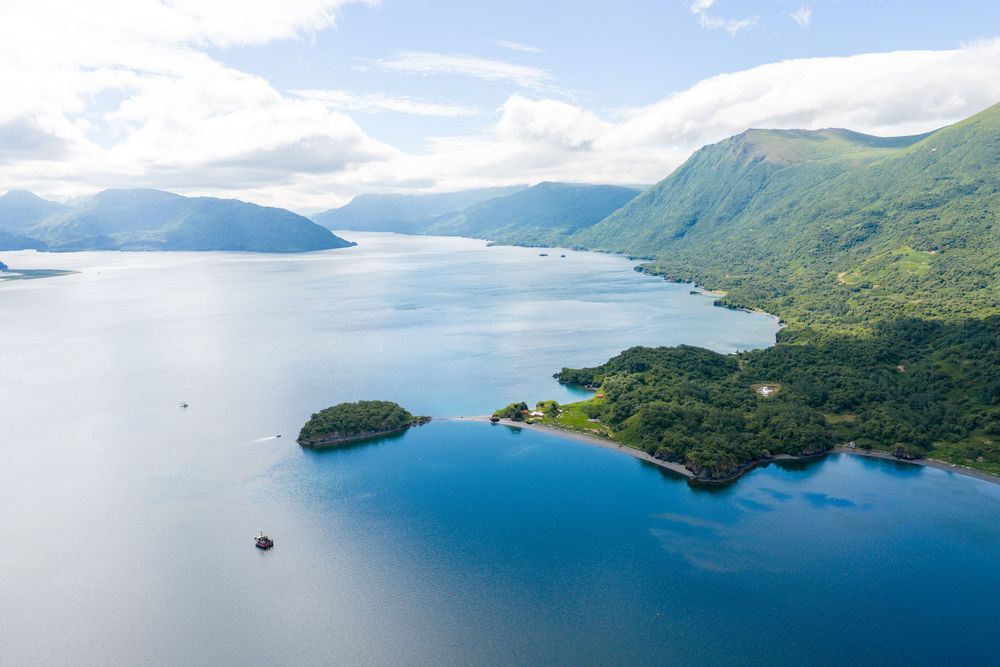 Aerial panoramic view of blue ocean waters meeting lush green mountains along a tropical coastline.