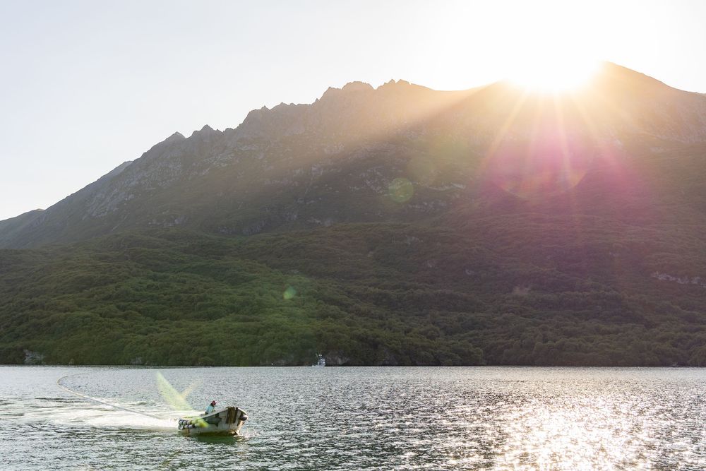 A series of panoramic images show a sunrise over mountains reflected in calm lake waters with a small fishing boat.