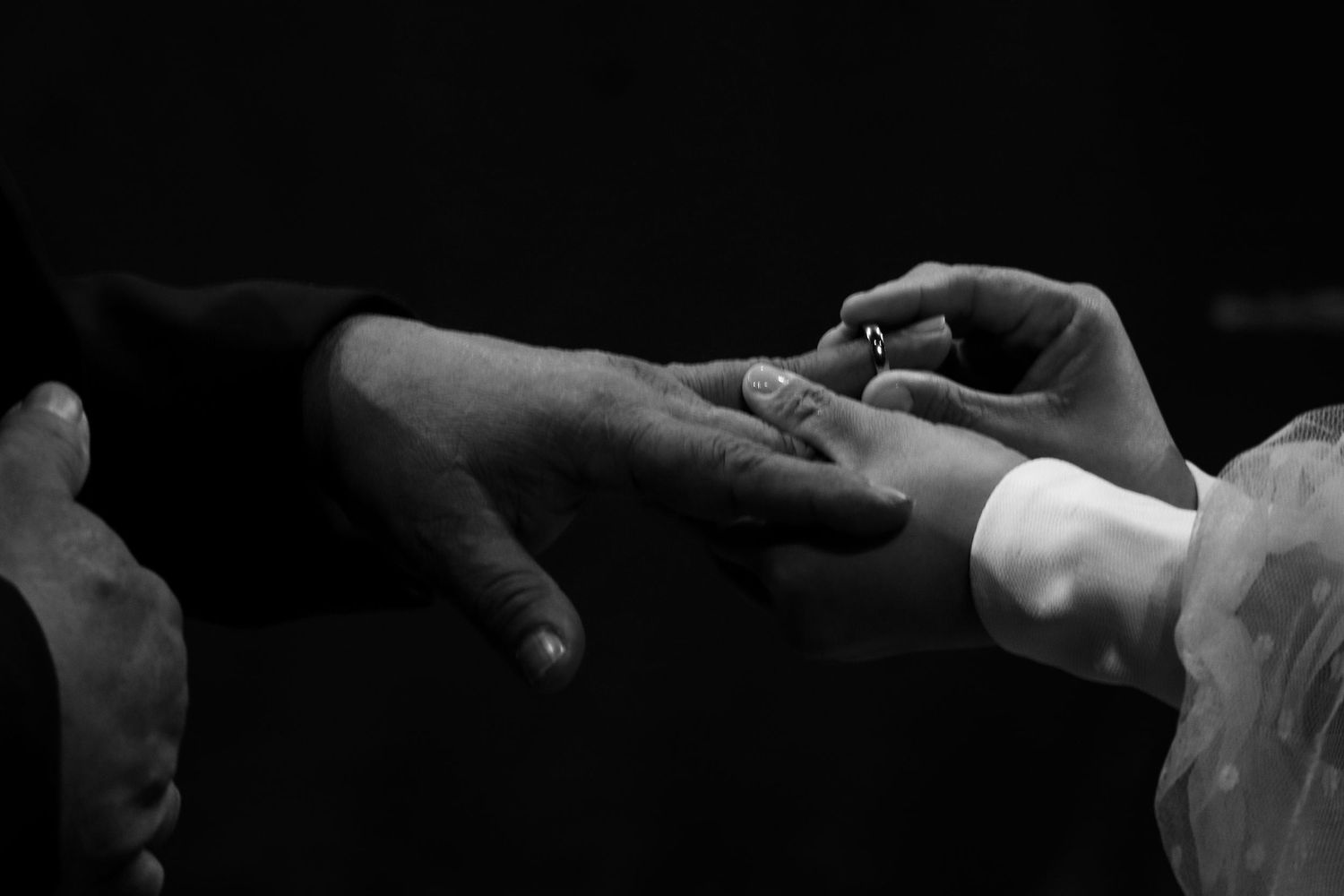Black and white close-up of hands exchanging a wedding ring during a marriage ceremony.