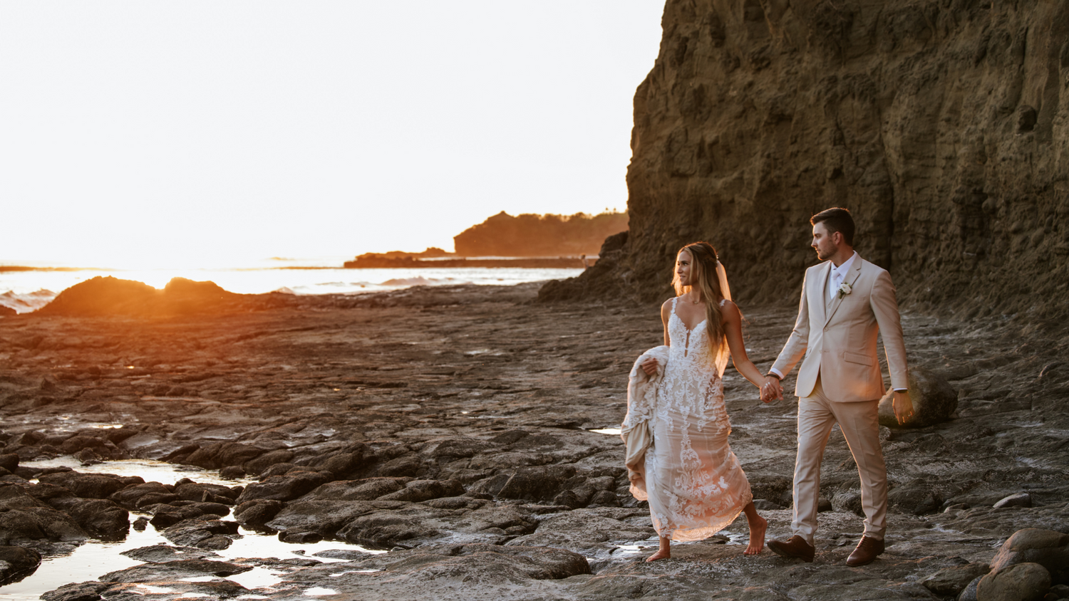 Romantic bride and groom portrait on the beach rocks at golden hour. in Punta Pita