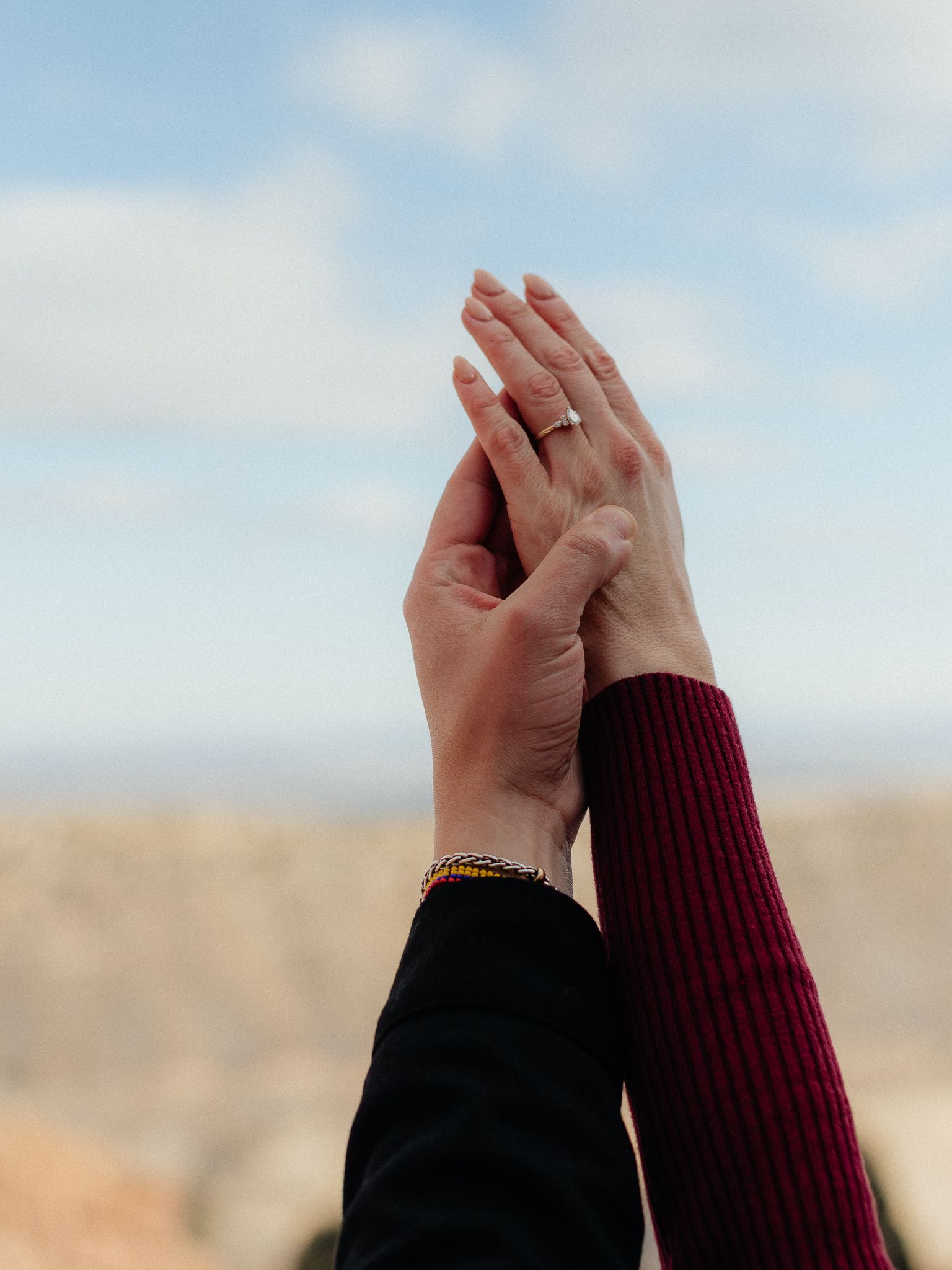 Two hands clap together against a bright blue sky and blurred desert landscape background.