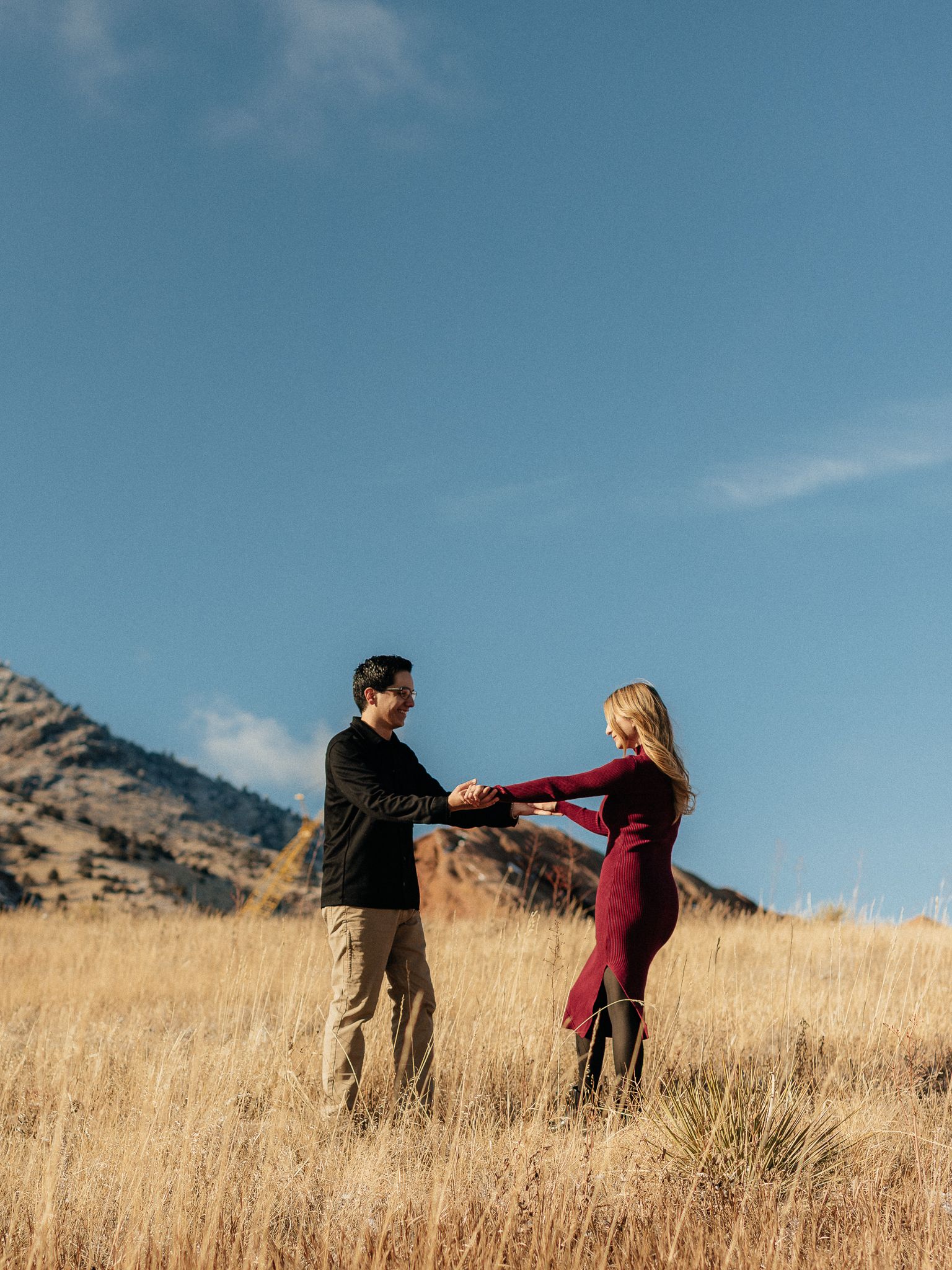 Two people dancing together in a golden field with mountains and blue sky in the background.