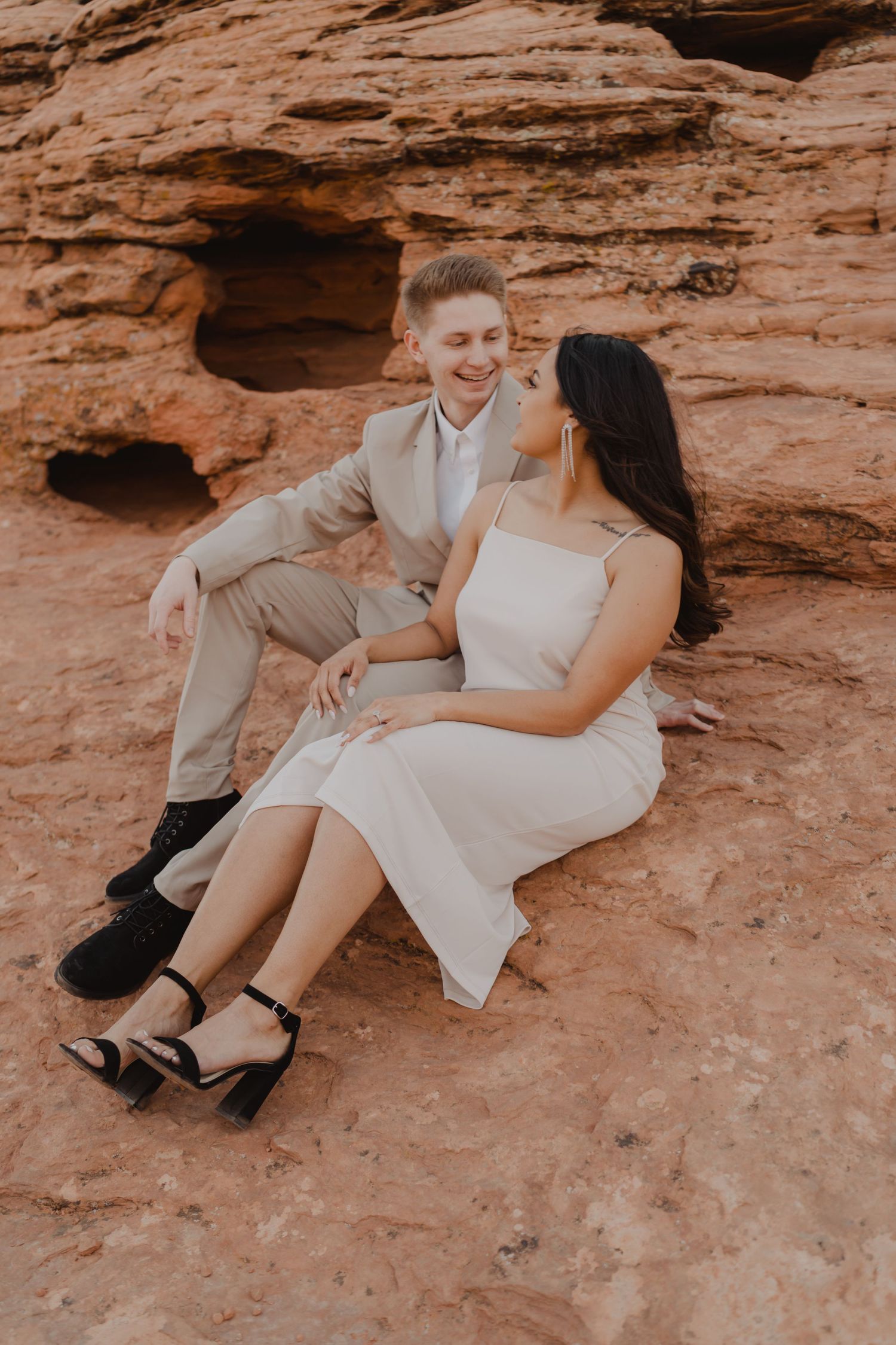 Couple in light colored outfits posing on red rock formations.