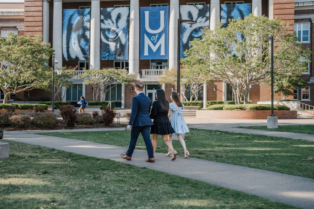 A couple walking together on a path in front of a university building on a sunny day.