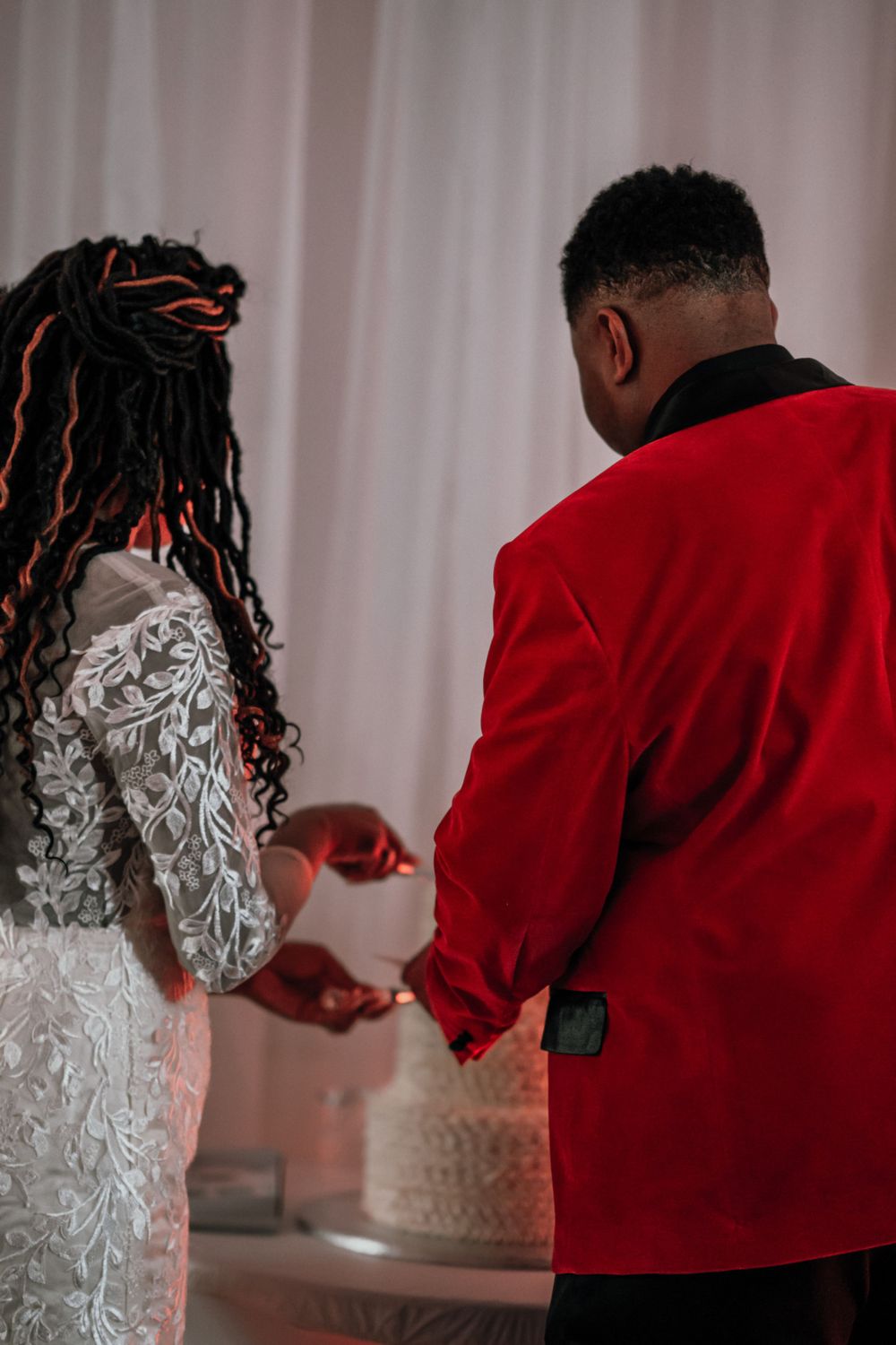 A couple in formal attire cutting their wedding cake together at their reception.