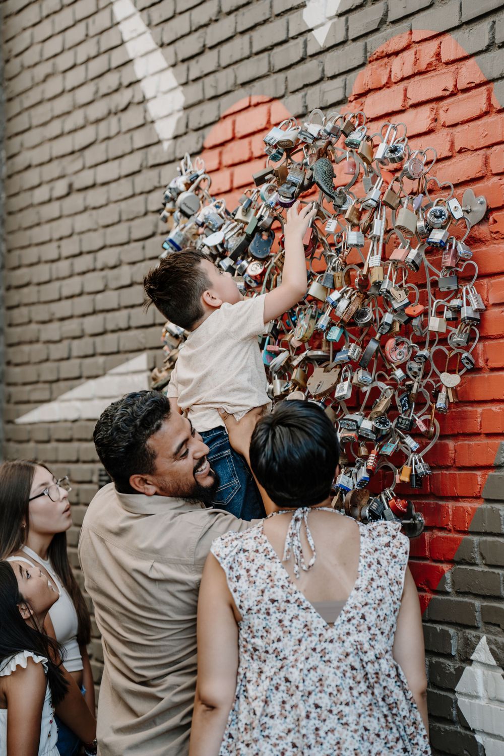 A family reaching up to interact with a decorative wall installation against red and gray brick.