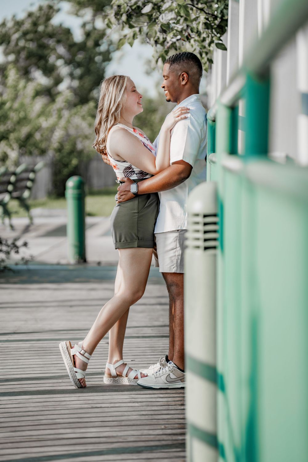 A couple shares a romantic moment on a wooden boardwalk surrounded by greenery.
