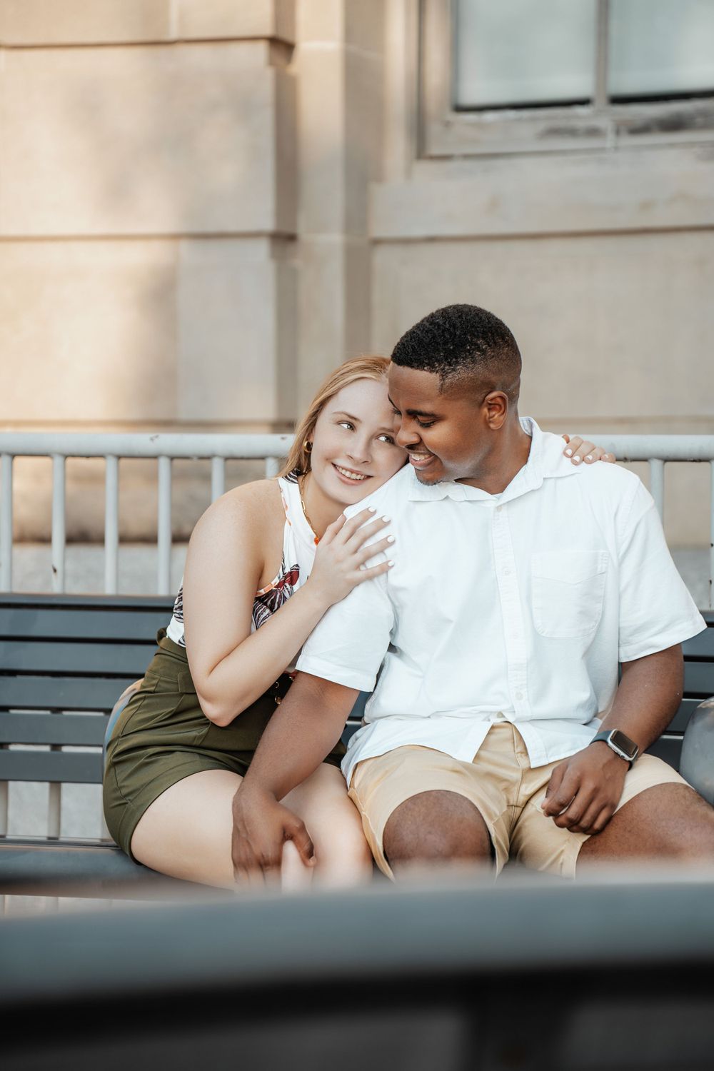 A couple shares an intimate moment while sitting together on an outdoor bench.