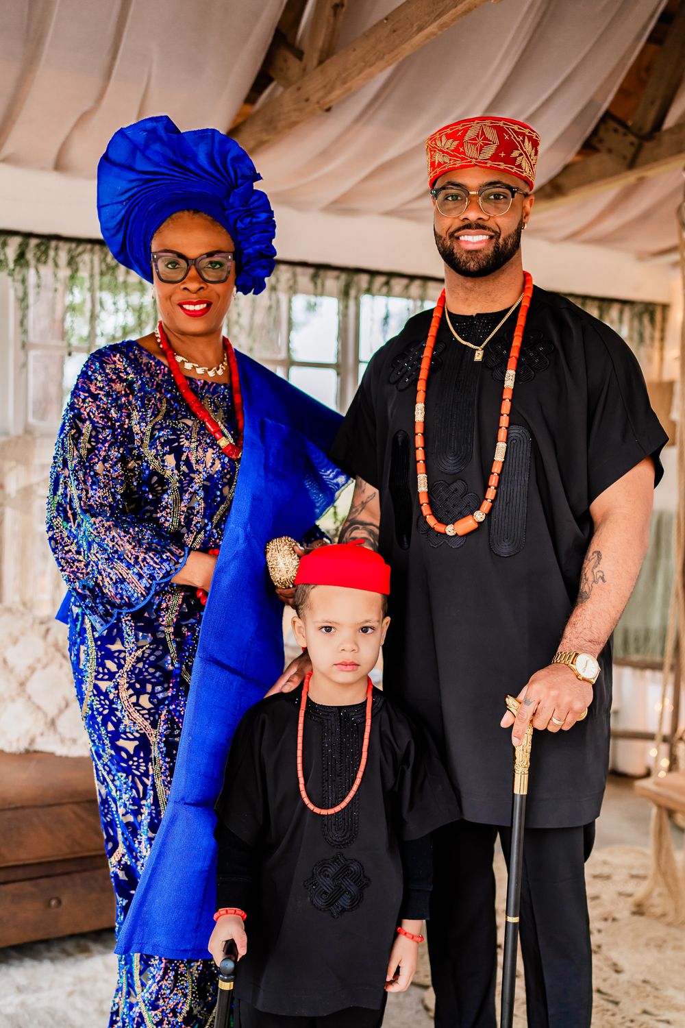 A family in traditional Nigerian attire poses together, wearing blue and black clothing with coral beads.