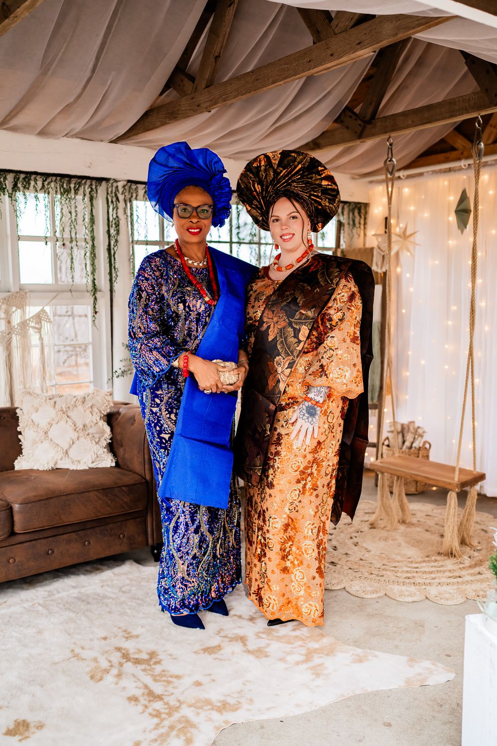 Two women in colorful traditional dresses stand together in a rustic interior setting with natural lighting.