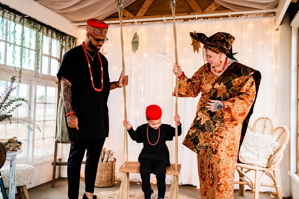 A family in traditional African attire plays together in a sunlit room with white curtains and rattan furniture.