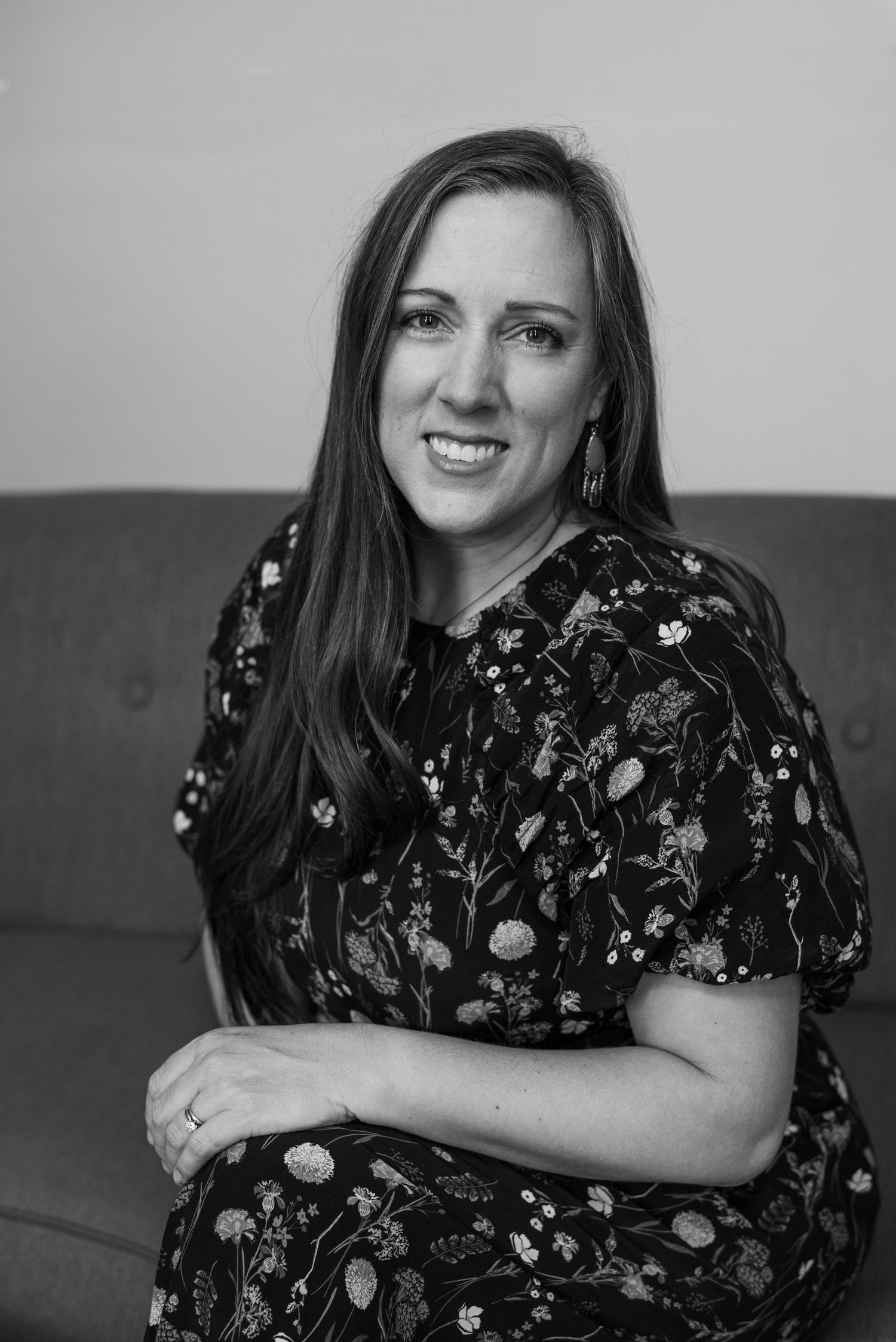 Portrait of Crystal Corona in floral dress seated on couch.