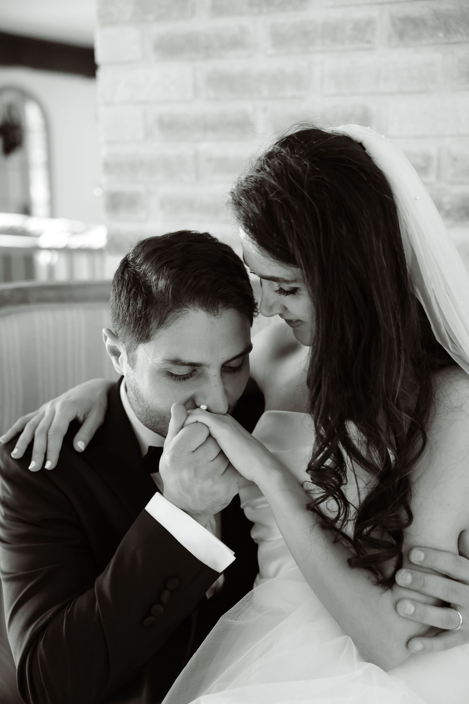Intimate black and white wedding moment captured against brick wall backdrop.