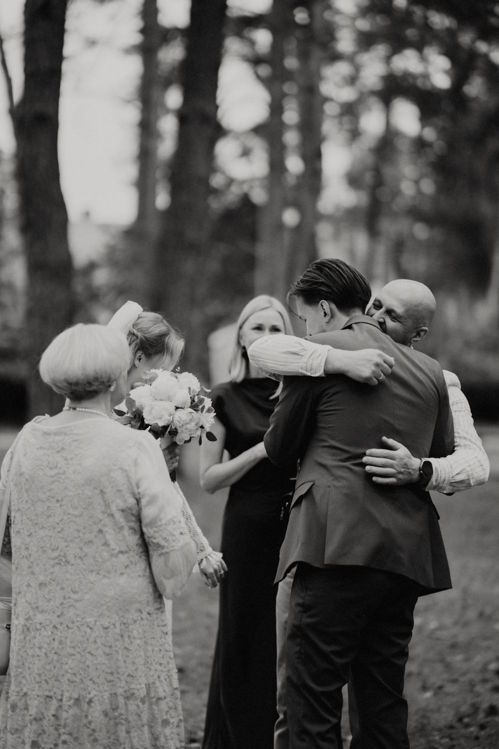 Wedding party members embrace in a group hug outdoors.