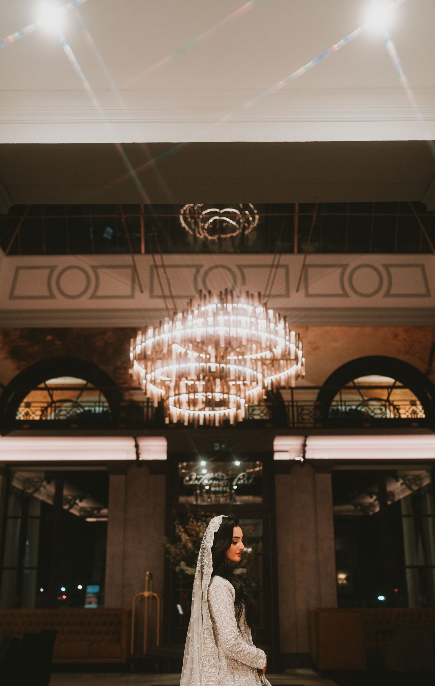Elegant bridal photo beneath grand crystal chandelier in historic venue.