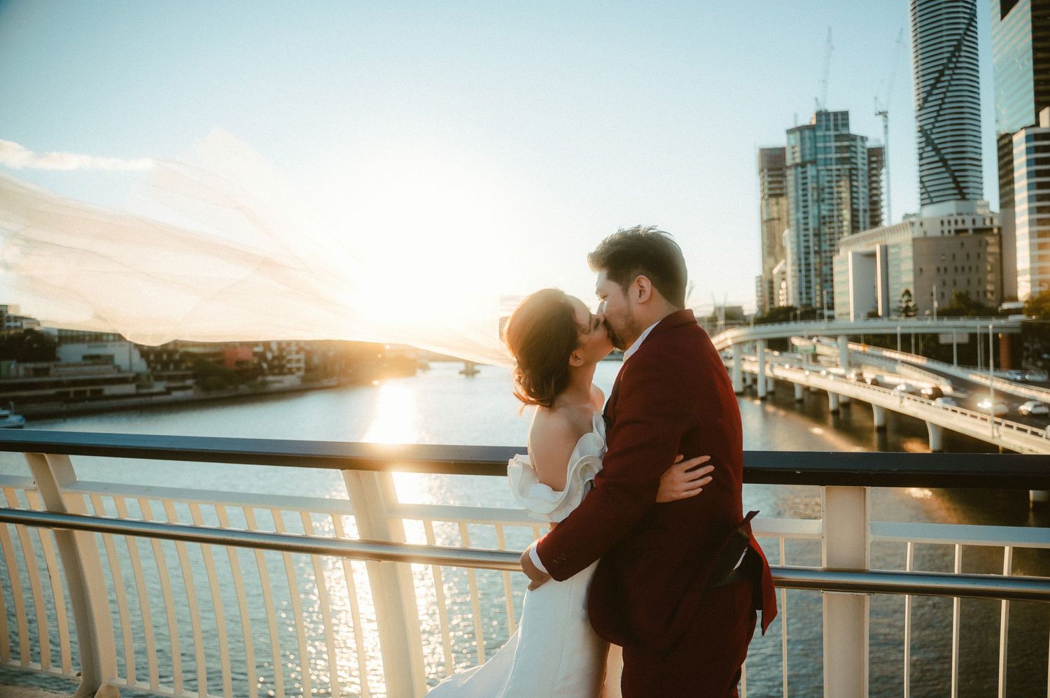 Couple embracing on waterfront pier during sunset with cityscape backdrop.