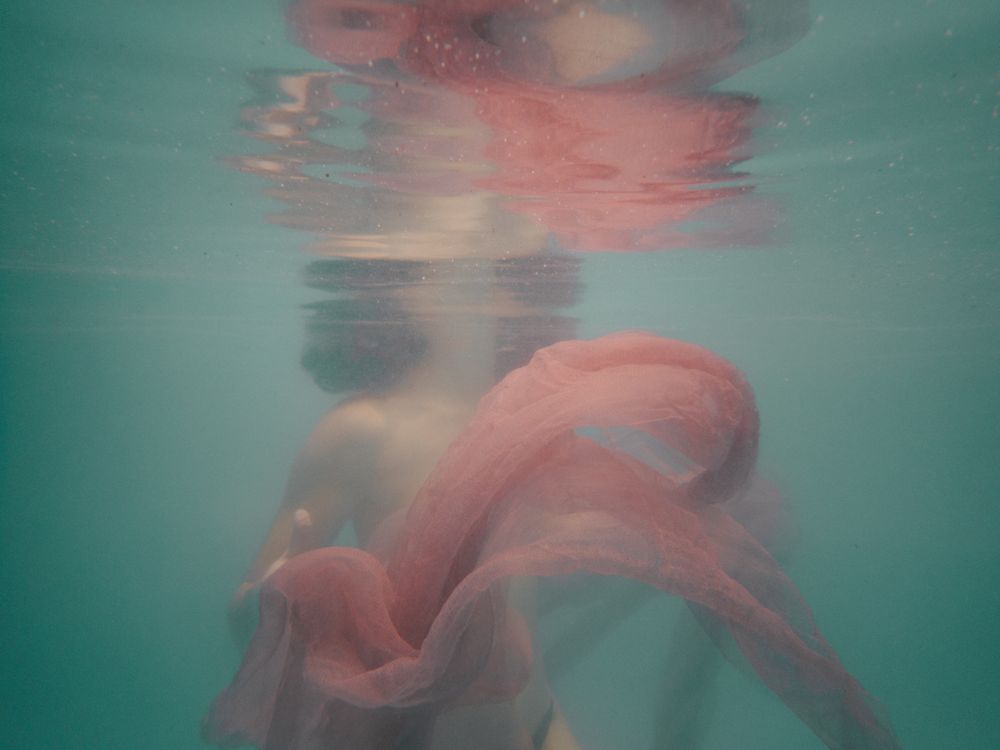 Underwater fashion photography with flowing coral fabric creating dreamlike effect.