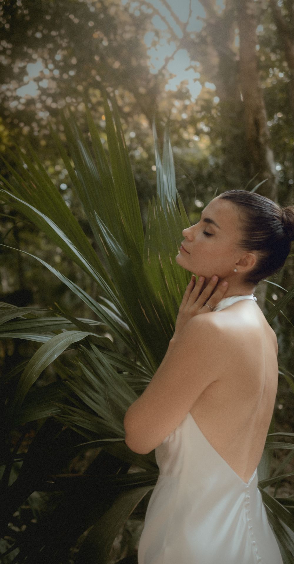 Artistic portrait in white dress against tropical foliage background.